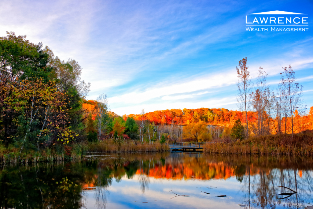 still flat water with orange and red trees behind it and a blue sky with streaky white clouds